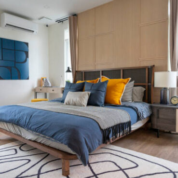 Yellow and blue pillow on cozy modern bedroom with carpet and side table lamp.